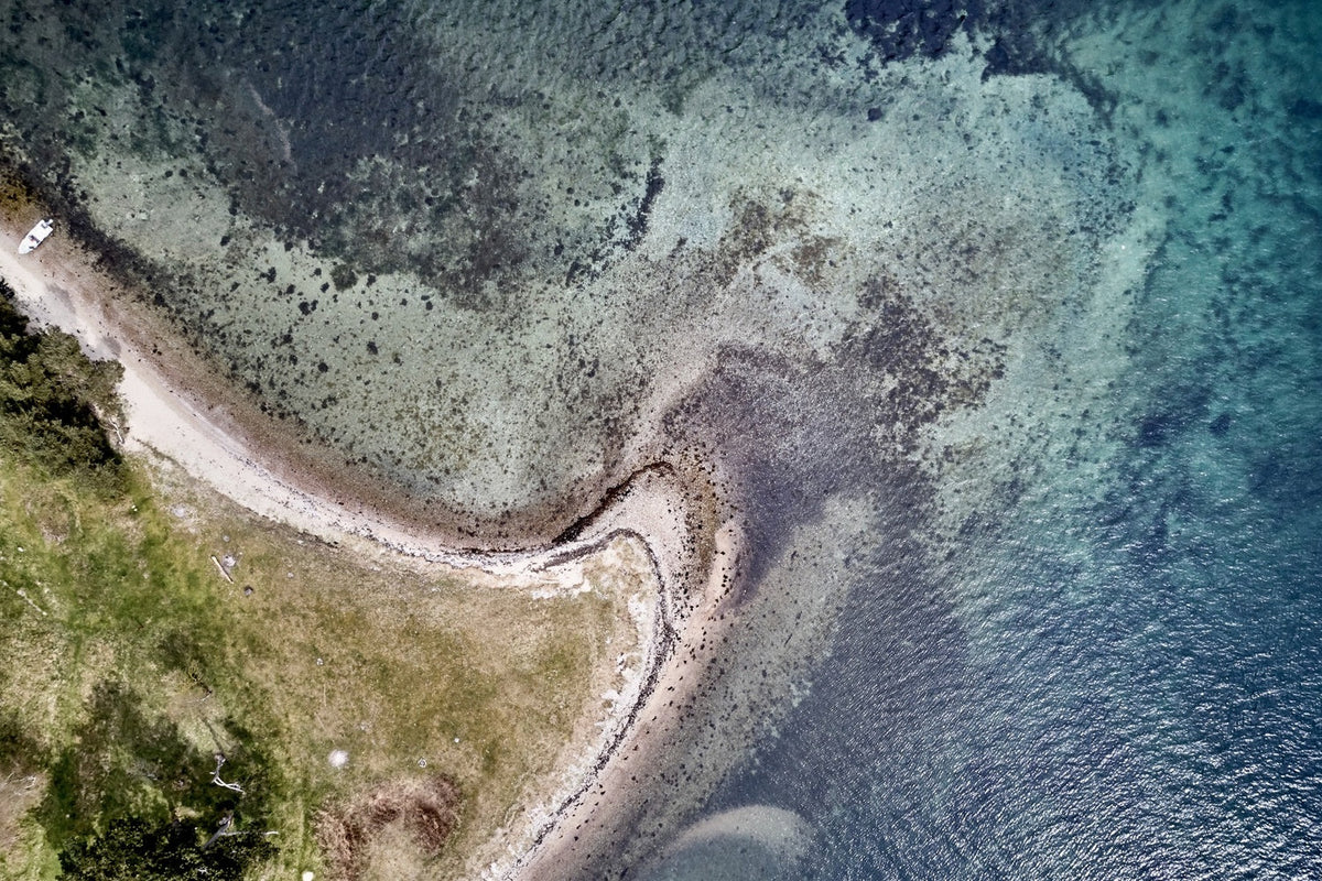 Luftfoto af havørredkyst med pynt, sandbund og mørke bundpartier